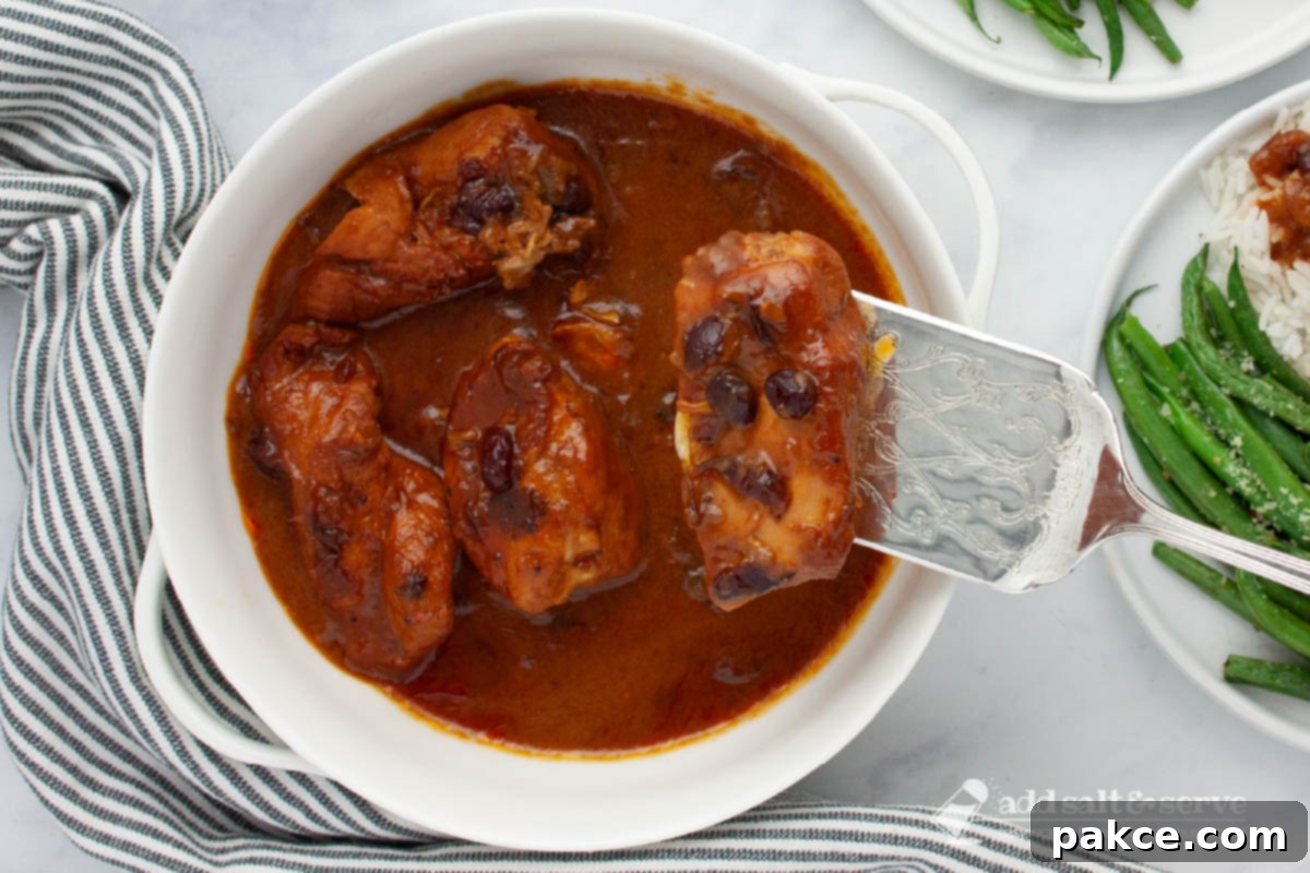 Slow Cooker Zesty Cranberry French Chicken 5 White serving dish with cooked chicken breasts in a sauce made from cranberry sauce with whole cranberries, French dressing, and onion soup mix with a single piece of chicken lifted on a spatula.