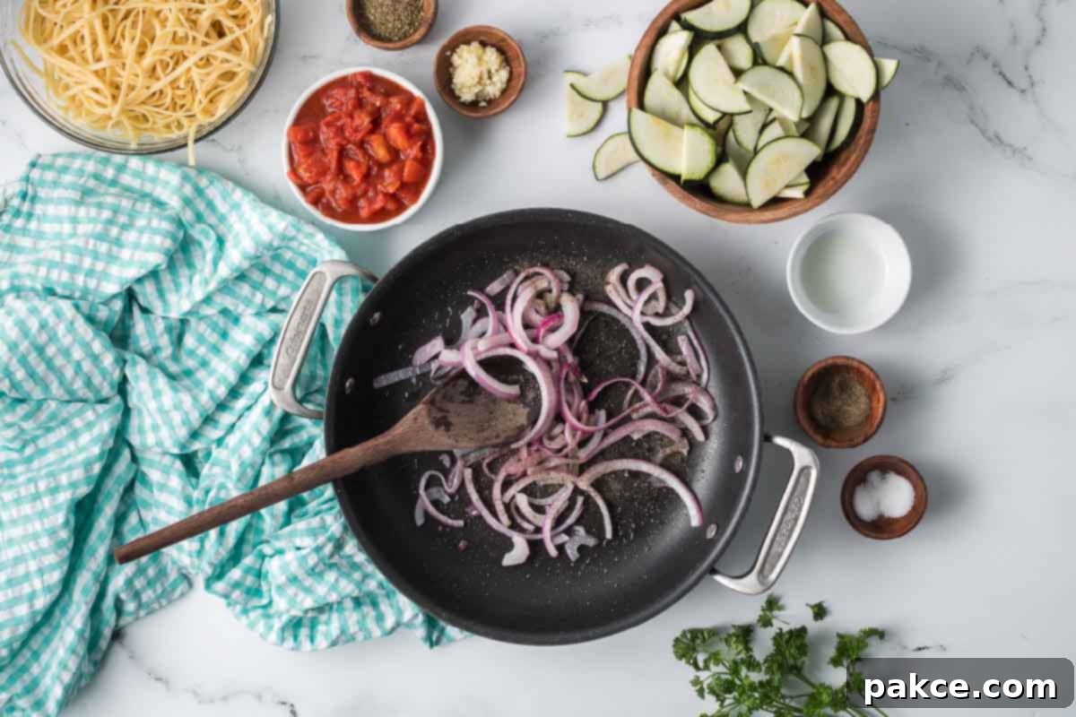 Spiralized Zucchini Linguine 5 Sliced red onion sautéing in a skillet surrounded by dishes of sliced zucchini, cooked linguine, minced garlic, Italian seasoning, salt, pepper, and diced canned tomatoes.