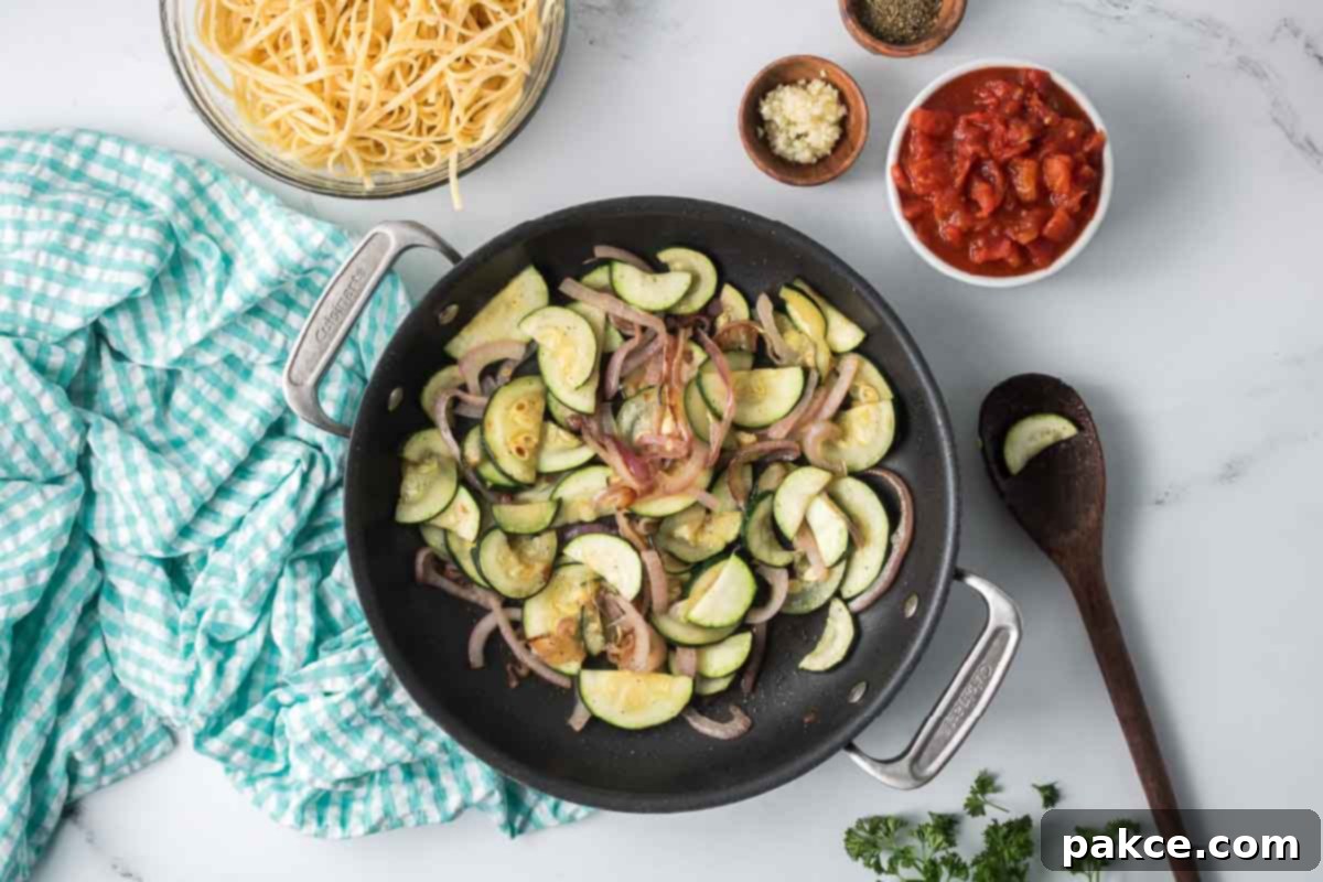 Spiralized Zucchini Linguine 6 Sliced zucchini and red onion sautéing in a skillet surrounded by dishes of cooked linguine, minced garlic, Italian seasoning, and diced canned tomatoes.