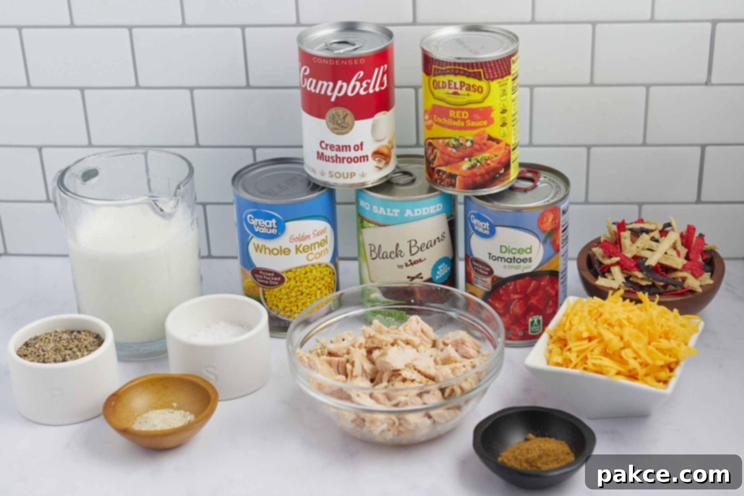15 Minute Creamy Chicken Enchilada Soup 3 A vibrant display of all the ingredients needed for Creamy Chicken Enchilada Soup, including milk, canned corn, black beans, diced tomatoes, cream of mushroom soup, red enchilada sauce, cooked chicken, and various seasonings, alongside garnishes.