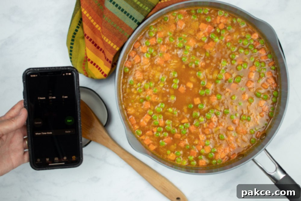 Vibrant Mexican Veggie Rice 7 In-process Restaurant Style Mexican Rice in a skillet, with a hand holding a phone using the timer, illustrating the simmering stage