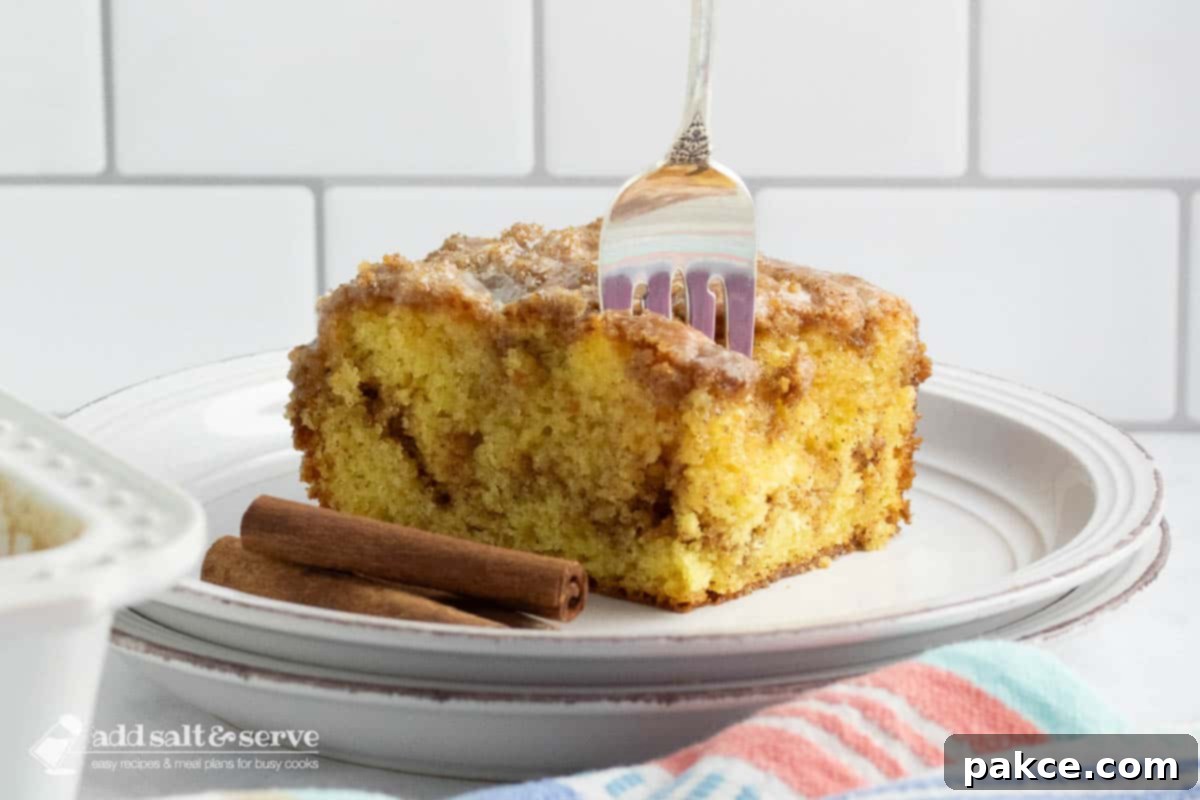 Slice of Honey Bun Cake on a plate showing the cinnamon swirl in the middle and vanilla glaze on top with a fork stuck in the top of the cake.