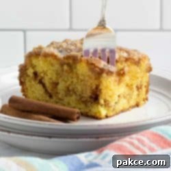 Honey-Glazed Cinnamon Swirl Cake 8 Slice of Honey Bun Cake on a plate showing the cinnamon swirl in the middle and vanilla glaze on top with a fork stuck in the top of the cake.