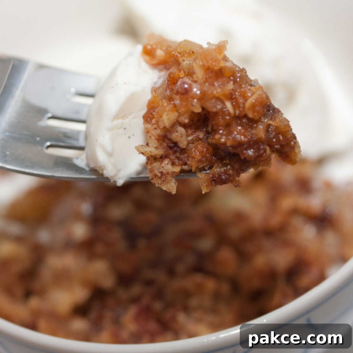 A fork picking up a bite of Apple Crumble topped with ice cream.