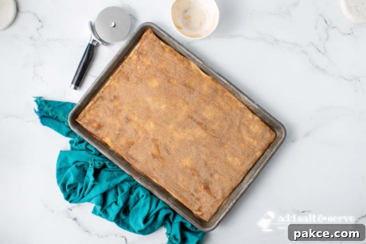Effortless Cinnamon Sticks from Pizza Dough 6 Pizza crust dough rolled out on a baking sheet and covered in melted butter and cinnamon sugar before baking.