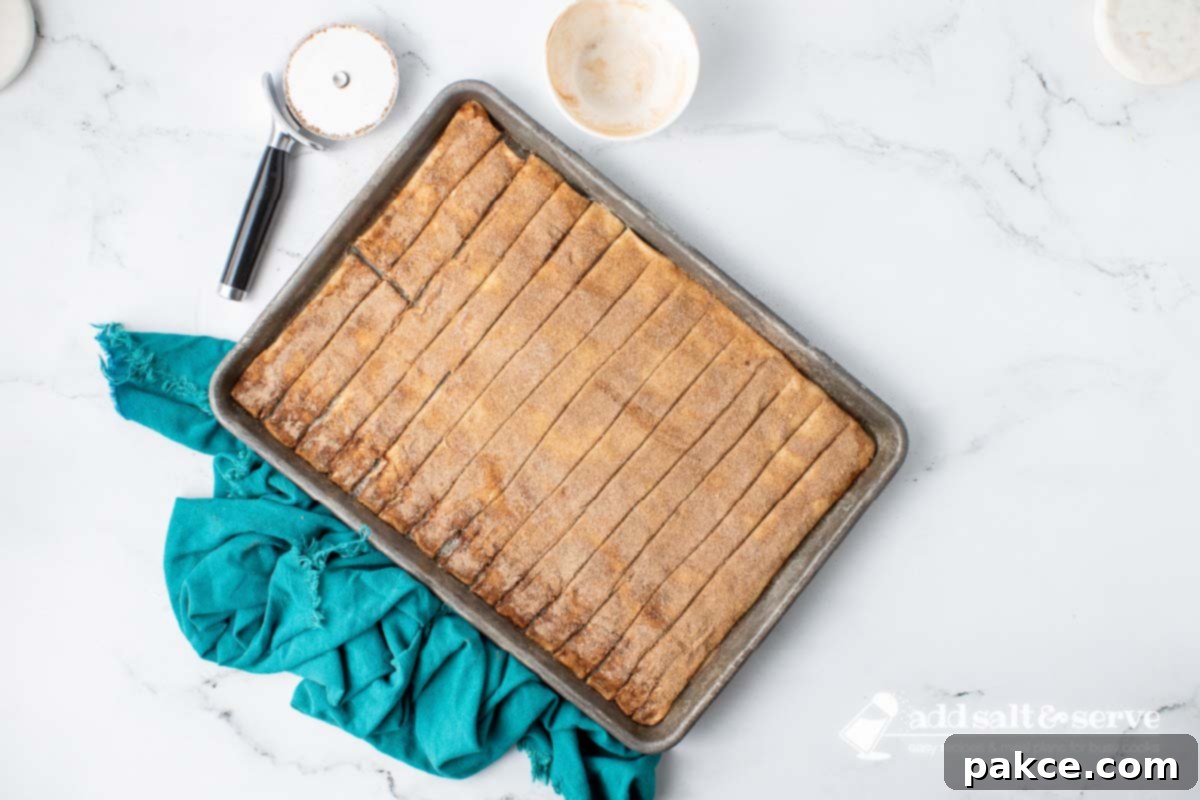 Effortless Cinnamon Sticks from Pizza Dough 7 Cinnamon sticks topped with butter and cinnamon sugar on a baking sheet before baking.