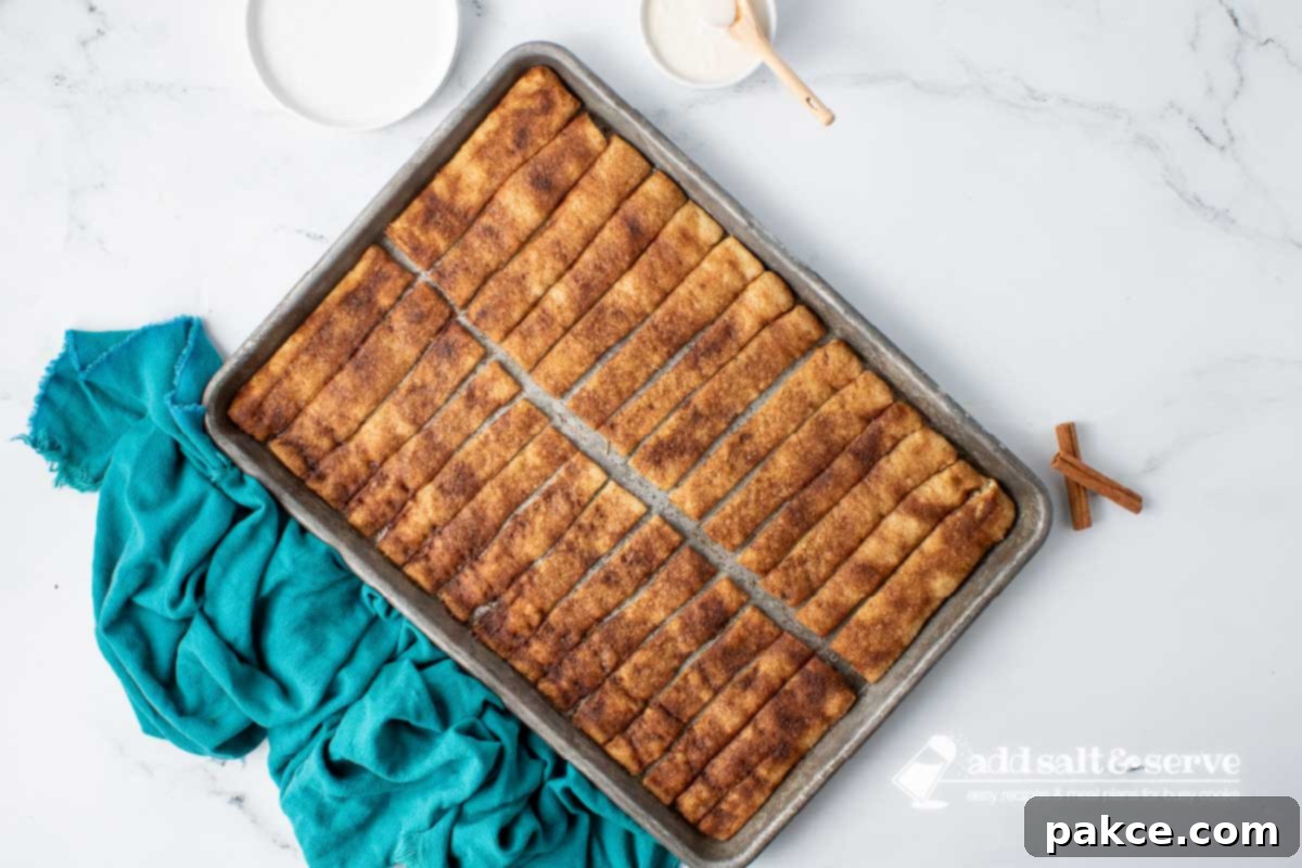 Effortless Cinnamon Sticks from Pizza Dough 8 Baked cinnamon sticks encrusted with cinnamon sugar in butter on a baking sheet.