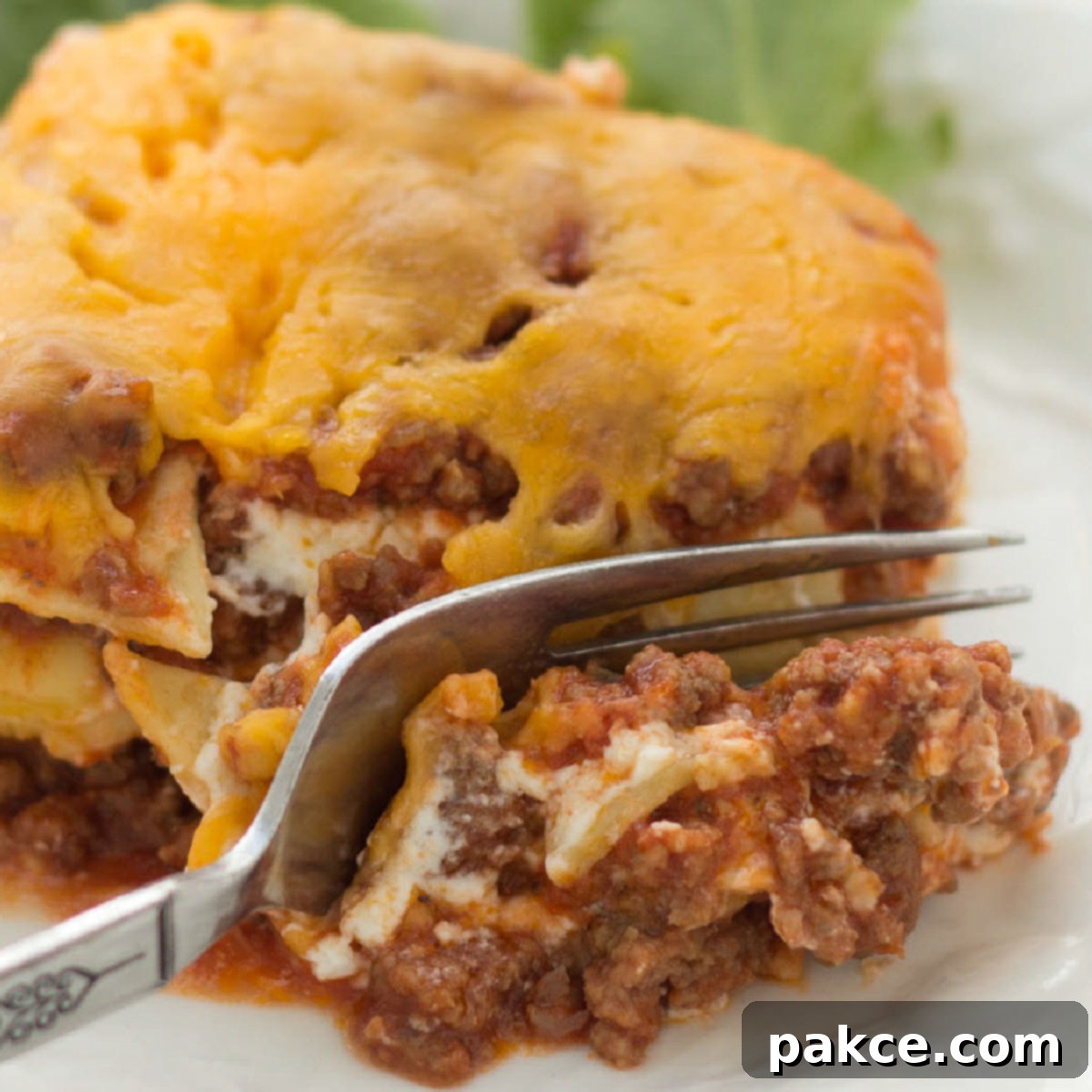 A slice of Layered Italian Beef Casserole being cut by a fork, showcasing the distinct layers of noodles, beef, and creamy cheese