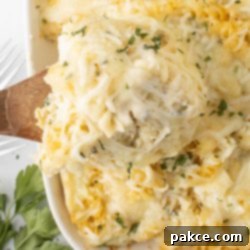 Creamy Alfredo Rotini Bake 13 Alfredo Rotini Pasta Bake in a baking dish with a spoonful scooped out on a wooden spoon, ready to be served.