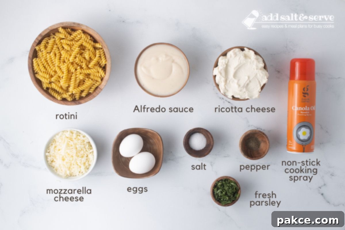 Creamy Alfredo Rotini Bake 3 Ingredients for Rotini Pasta Bake laid out: uncooked rotini pasta, a jar of Alfredo sauce, containers of ricotta and mozzarella cheese, eggs, salt, black pepper, fresh parsley, and a can of non-stick cooking spray.