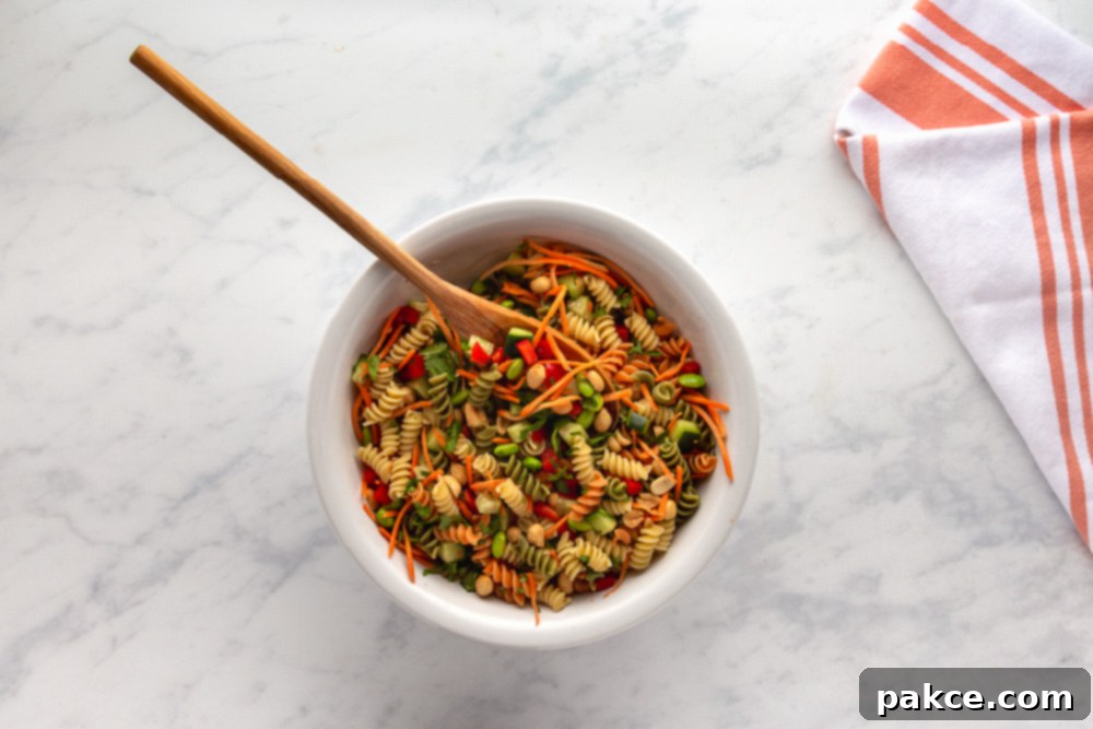 Thai Pasta Salad with Sesame Ginger Dressing 7 Mixing colorful pasta, vegetables, and peanuts in a large bowl for Thai Pasta Salad