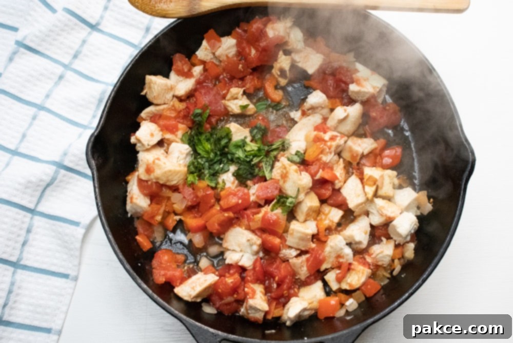 Mediterranean Chicken with Pasta Cast iron skillet cooking chopped chicken, diced tomatoes, and fresh basil