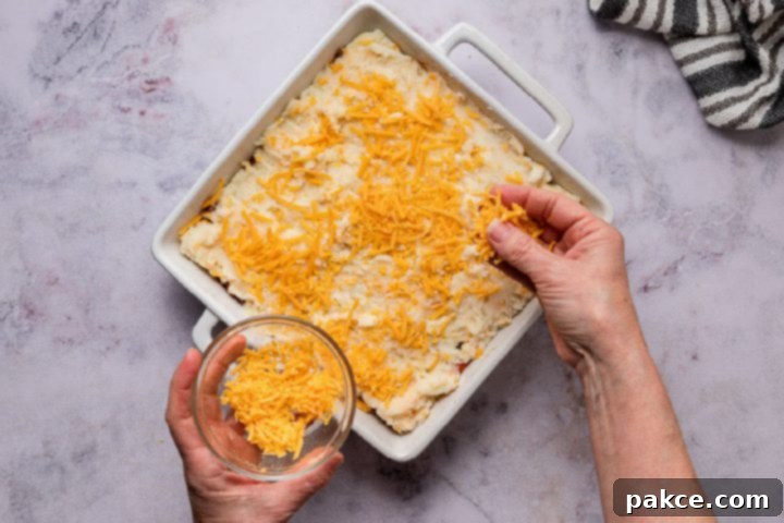 Freeze and Feast Shepherds Pie 9 sprinkling cheese on top of shepherd's pie before baking