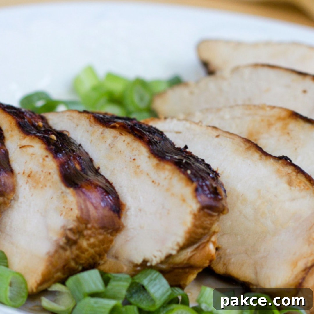 Perfectly sliced, juicy grilled chicken breast on a white plate, elegantly garnished with freshly chopped green onions, ready to serve or store.