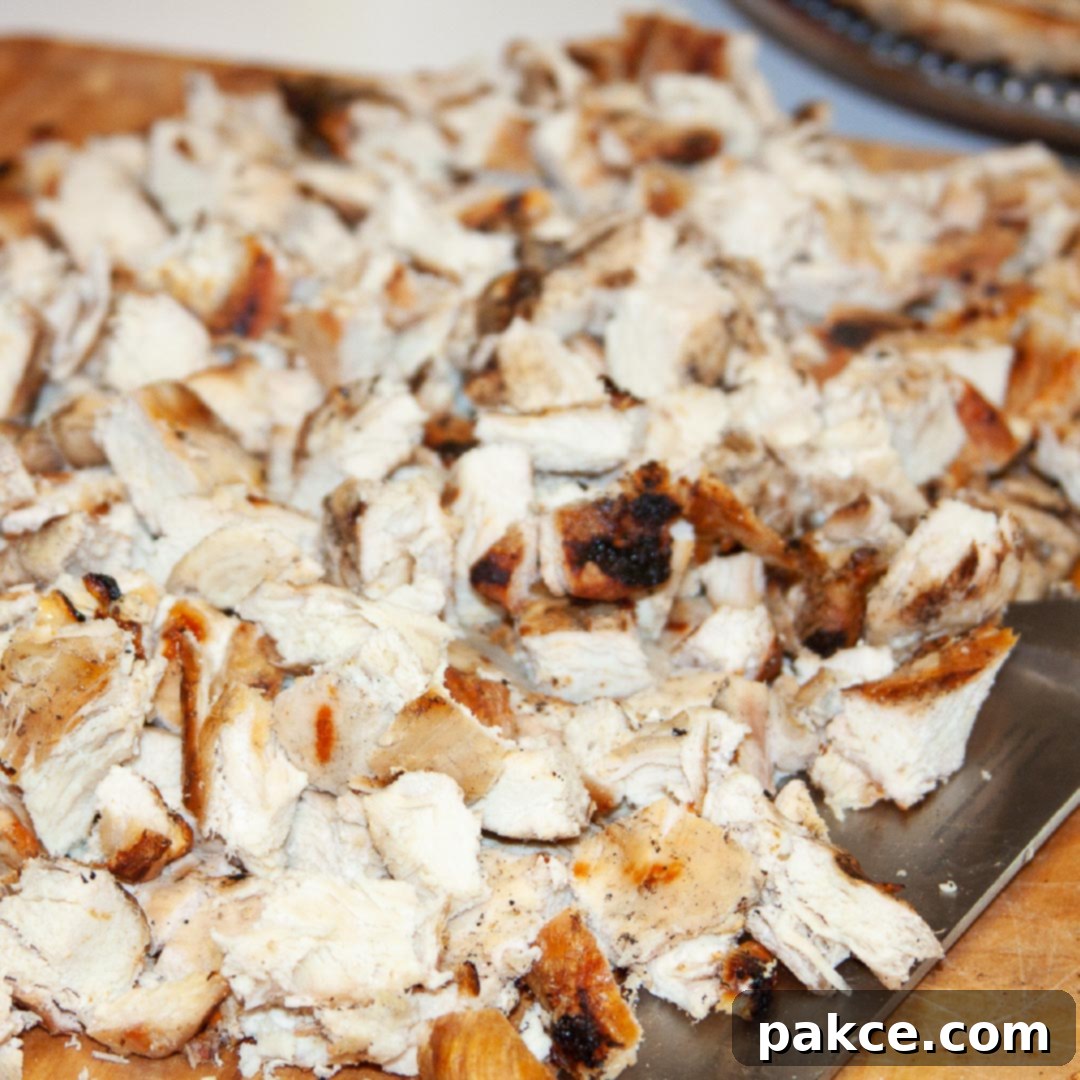 Expertly chopped grilled chicken resting on a wooden cutting board next to a sharp chef's knife, perfectly portioned and ready for convenient freezing.