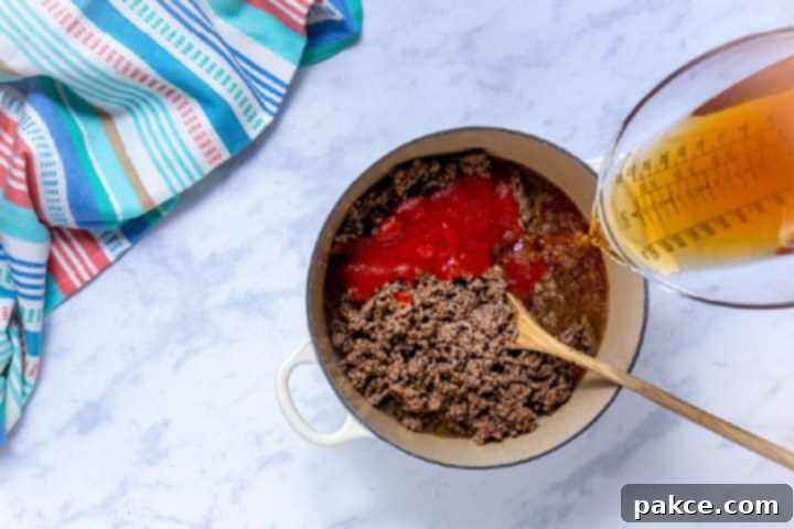 The Legend of Terlingua Chili 7 Adding tomato sauce and beef broth to the cooked ground beef in a Dutch oven, creating the chili base.