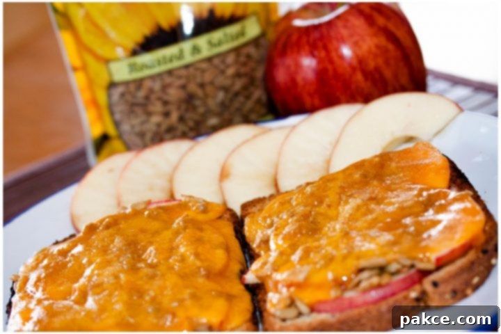 Open-faced Apple Cheddar Melt Sandwich with bread, mayo, apple slices, sunflower seeds, and cheddar melted on top and text Apple Cheddar Melt: Add Salt & Serve