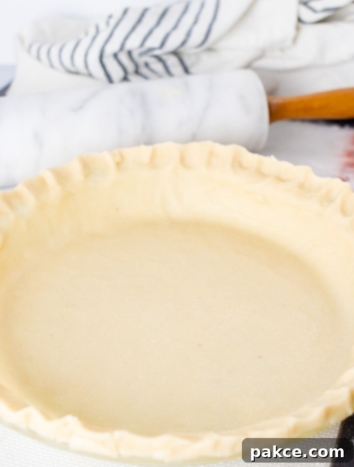 Unbaked pie crust in a pie pan ready for filling, with a marble rolling pin and a white flour sack towel in the background, illustrating the simplicity and elegance of homemade baking.