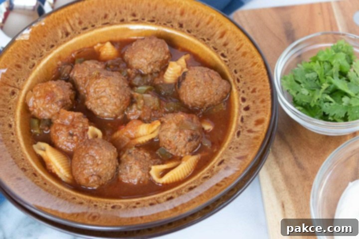 Photo is a brown soup bowl with meatball soup, beside a cutting board. On the cutting board are two clear glass bowls with parsley and sour cream.
