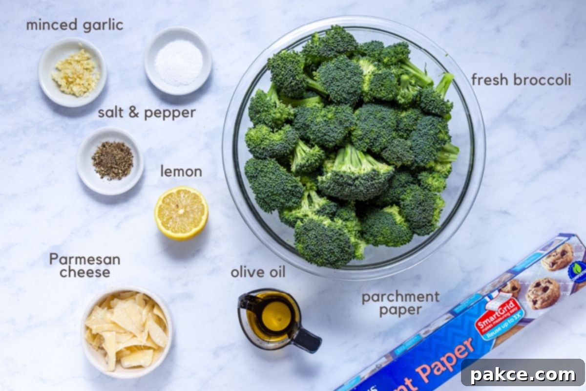 Garlic Roasted Broccoli 3 A vibrant collection of fresh ingredients for Roasted Garlic Broccoli: a large bowl brimming with crisp broccoli florets, small separate bowls holding minced garlic, coarse salt, freshly ground black pepper, and shaved Parmesan cheese. Alongside, a golden measuring cup of extra virgin olive oil and a bright lemon half add to the visual appeal. A roll of parchment paper sits ready for preparation.