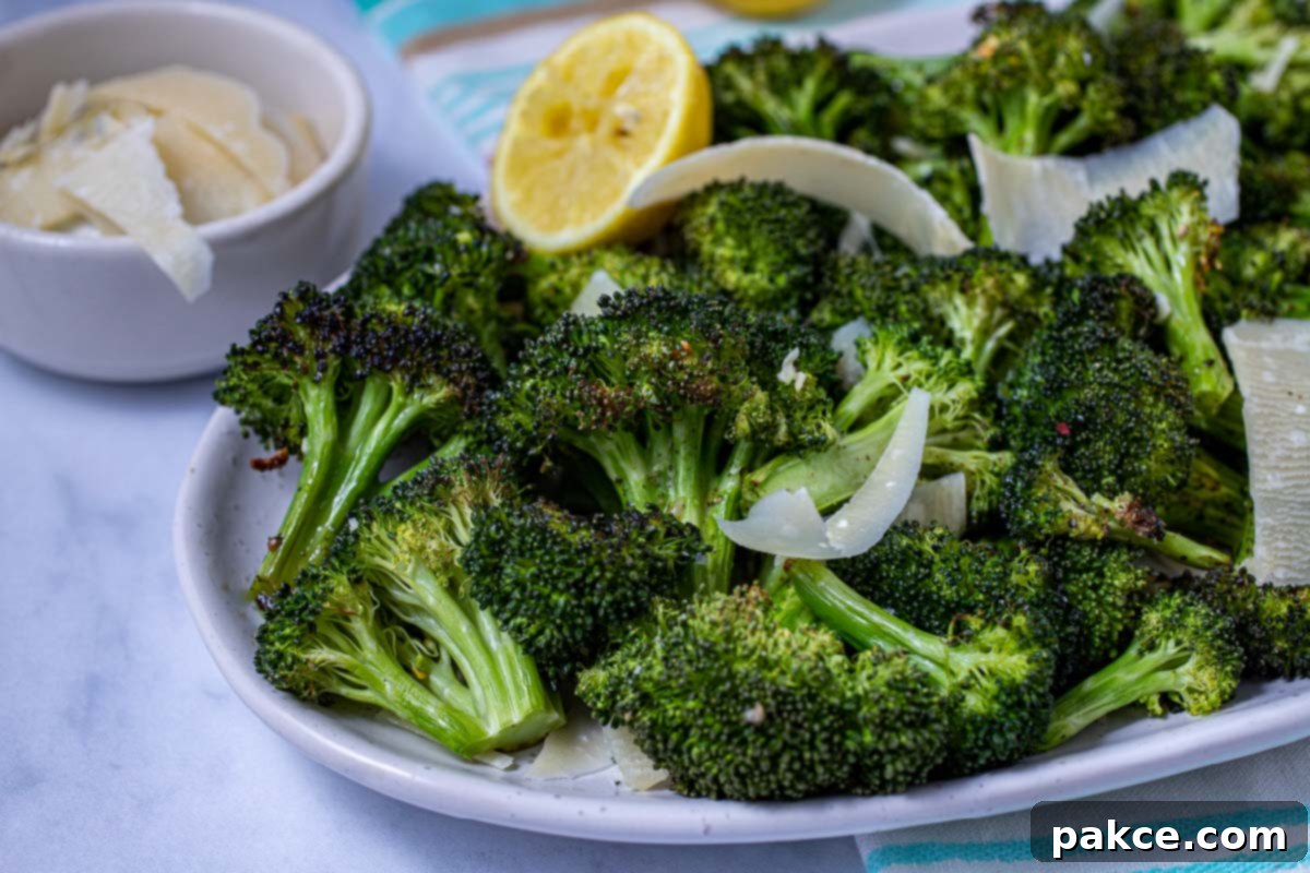 Garlic Roasted Broccoli 10 A serving plate filled with roasted garlic broccoli, ready to enjoy, accompanied by a lemon half and a small bowl of Parmesan cheese.