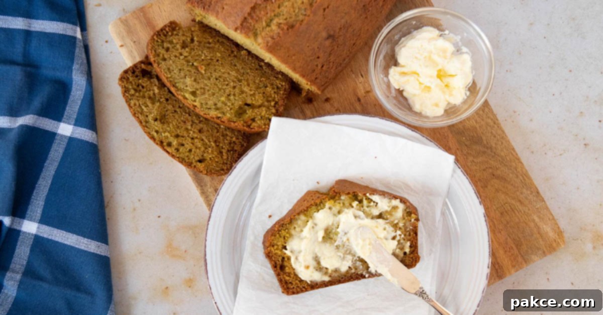 Overhead shot of a loaf of zucchini bread with a slice being spread with clotted cream, highlighting its moist texture and golden crust.