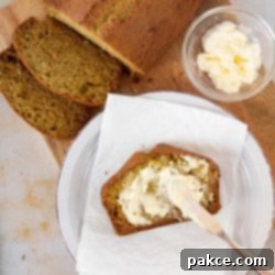 Effortless Zucchini Loaf 4 Overhead shot of a full loaf of moist zucchini bread, with a slice already cut and being spread with rich clotted cream, against a rustic backdrop, emphasizing its homemade appeal.