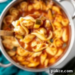 Hearty Tortellini Zucchini Soup 7 Ladleful of vibrant Tomato Zucchini Soup with tortellini, held over a simmering pot, ready to be served.