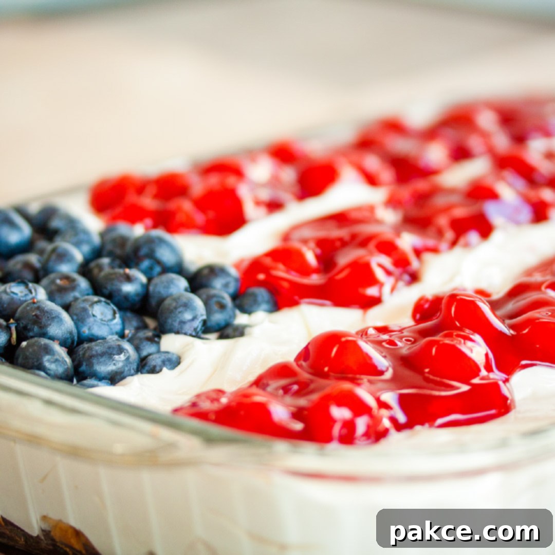 Fluffy white whipped cream mix over crumbled angel food cake topped with blueberies and cherry pie filling in the design of an American flag in a 9x12 glass pan