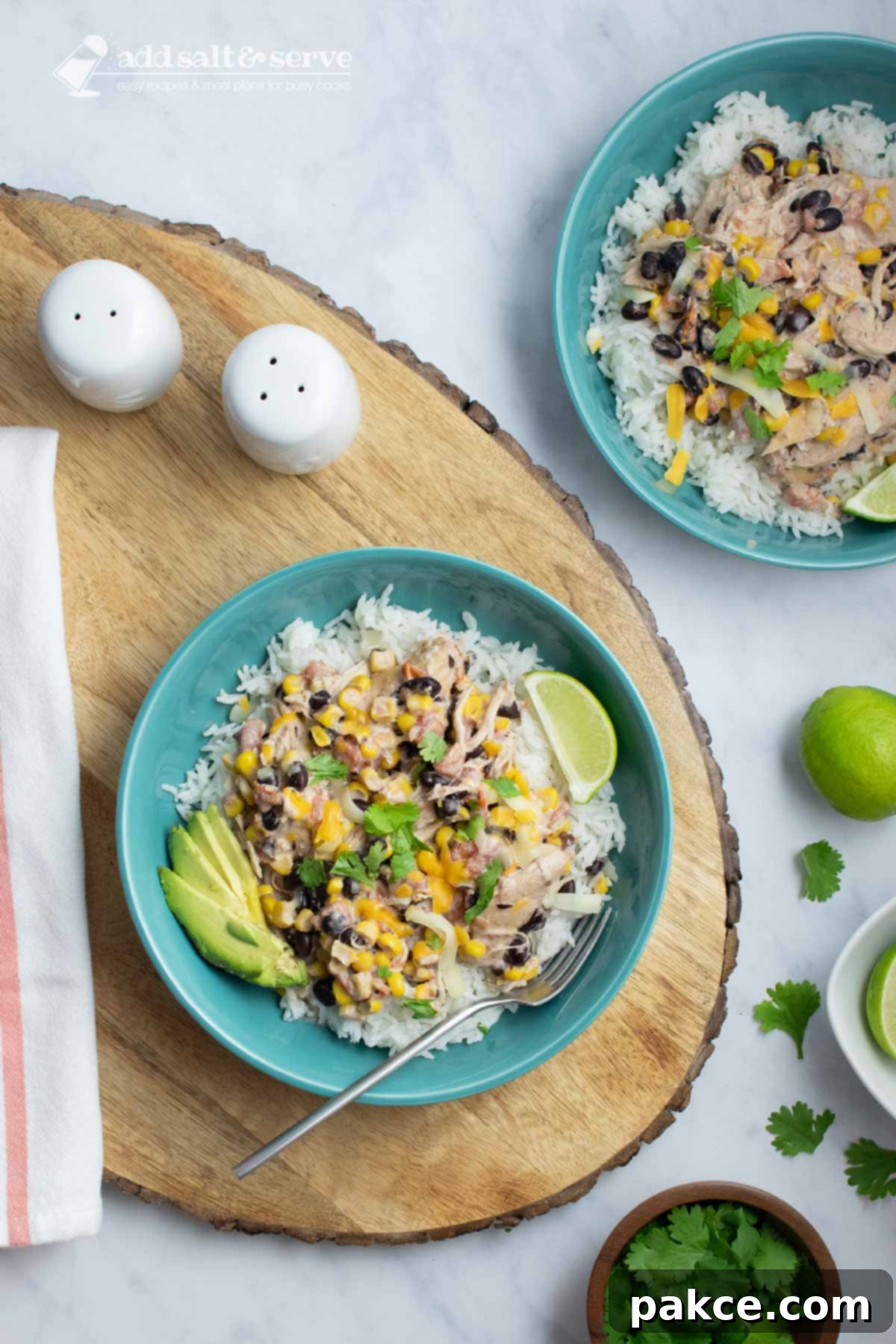 Celebration Chicken Pot 6 Bowl of shredded chicken in a creamy sauce with black beans, corn, tomatoes, and green chilies over rice and garnished with sliced avocado, shredded cheese, fresh cilantro, and lime wedges.