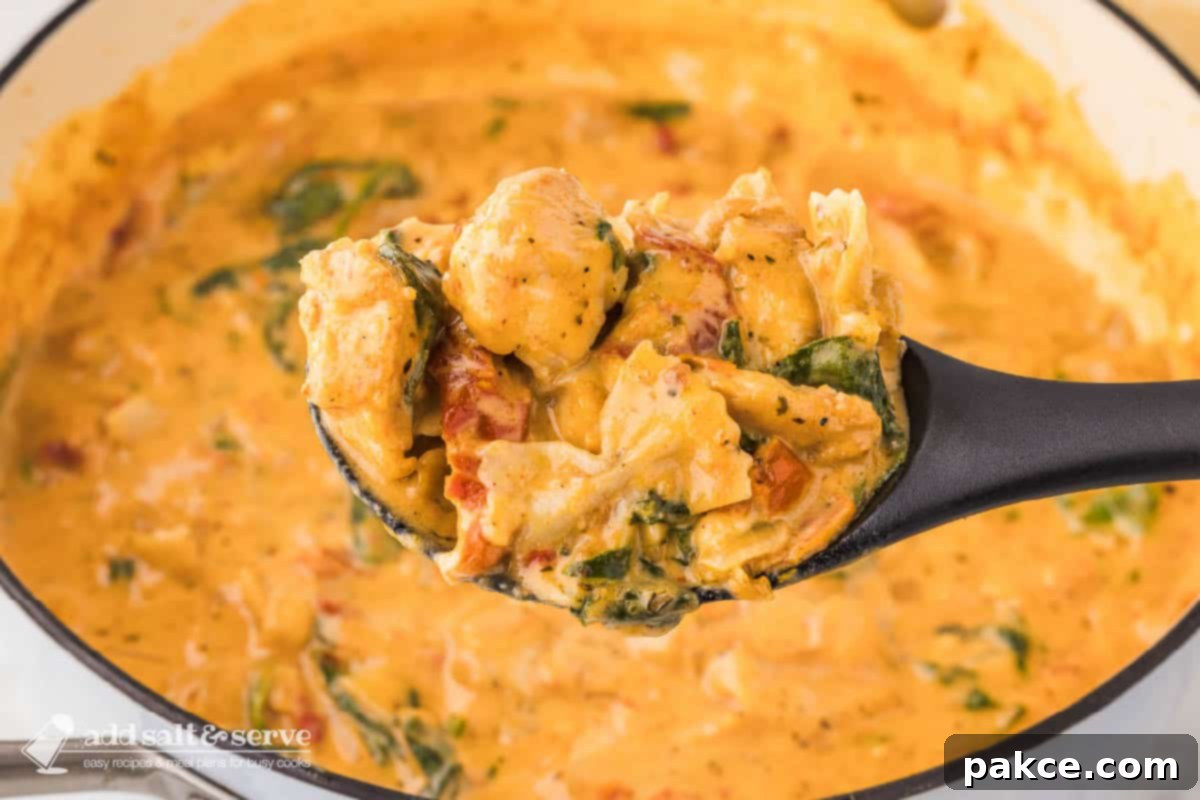 Creamy Tuscan chicken with sun-dried tomatoes, spinach, and mini farfalle in cream sauce in a pot with a serving on a spoon held over the pot and text Creamy Tuscan Chicken with Sun-dried Tomatoes.