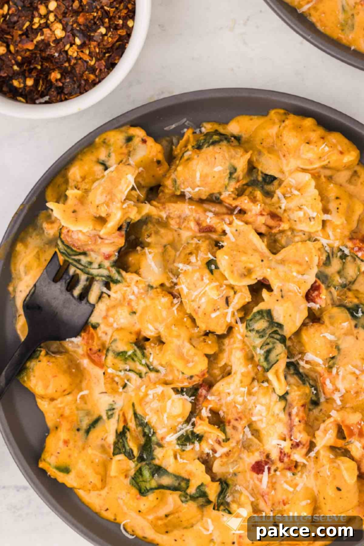 Velvety Tuscan Chicken with Sun-Kissed Tomatoes 6 Creamy Tuscan chicken with sun-dried tomatoes, spinach, and mini farfalle in cream sauce on a plate with a forkful on a fork resting on the plate.