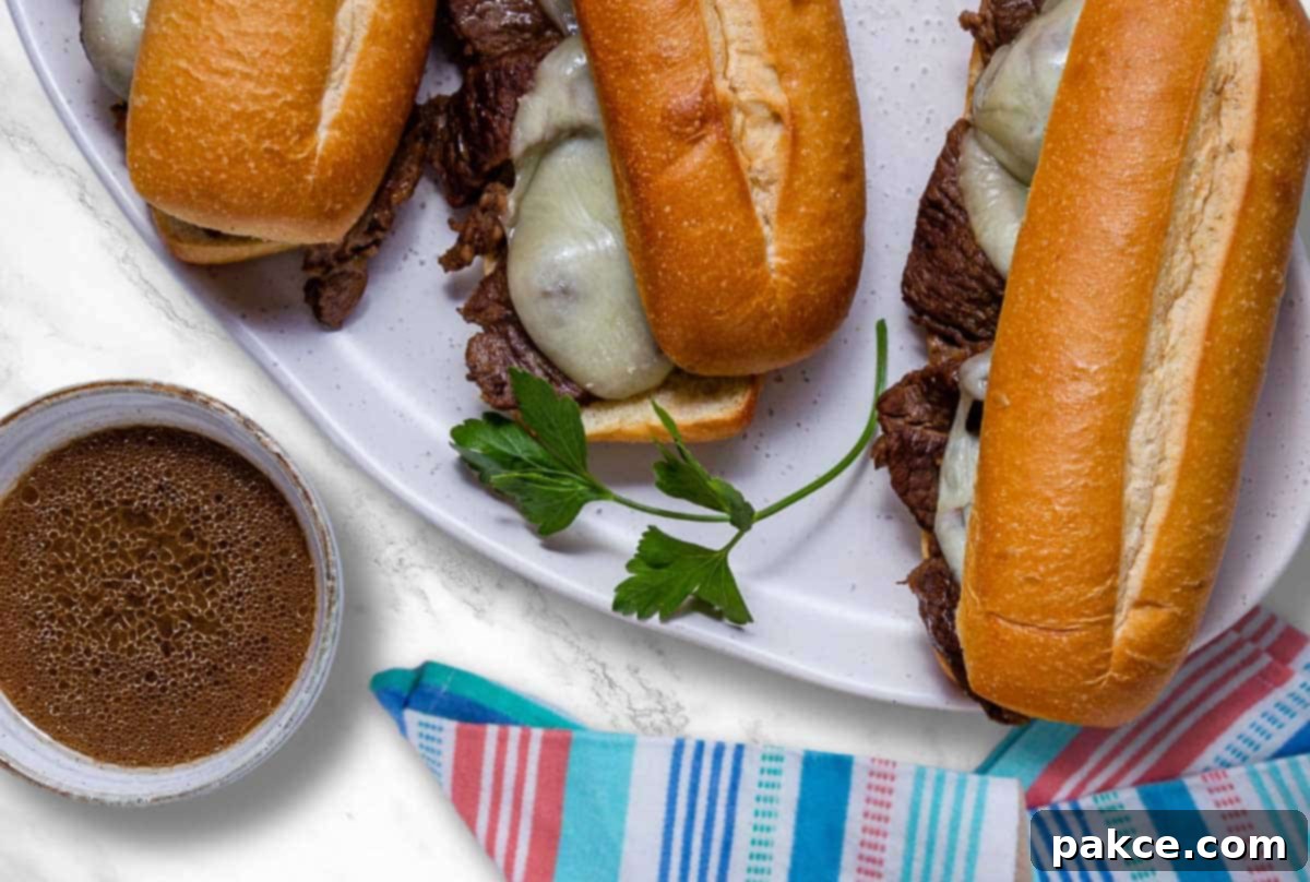 A plate of French Dip sandwiches beside a bowl of au jus, garnished with fresh parsley.