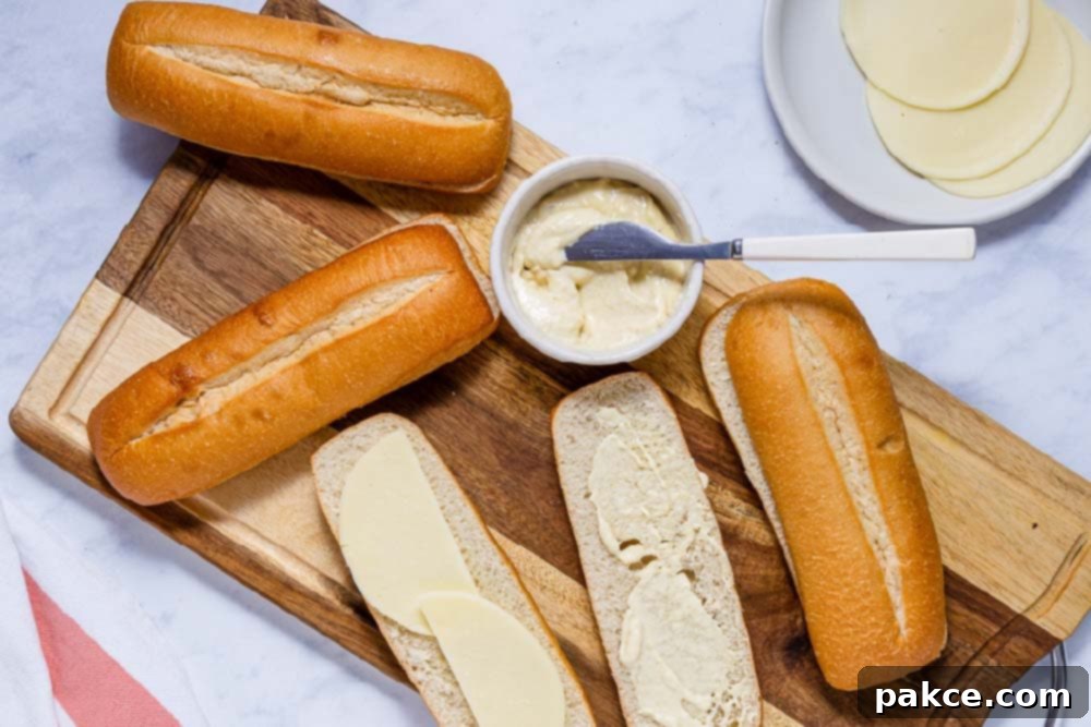 Easy Juicy Crockpot French Dip Sandwiches with Au Jus 5 Hoagie rolls sliced lengthwise on a cutting board with provolone cheese on one side and horseradish sauce on the other side.