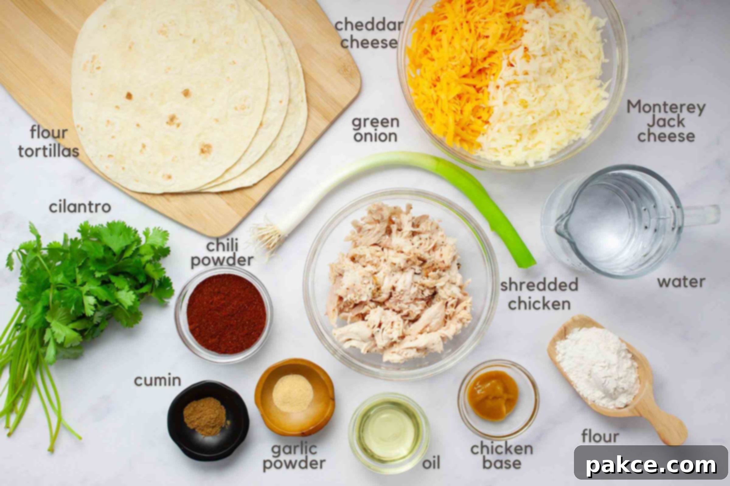 Effortless Layered Chicken Enchilada Casserole 3 A vibrant selection of ingredients for layered chicken enchilada bake on a kitchen counter, including flour tortillas, shredded cheddar and Monterey Jack cheeses, shredded rotisserie chicken, a fresh green onion, cilantro, chili powder, ground cumin, garlic powder, vegetable oil, chicken base, all-purpose flour, and water.