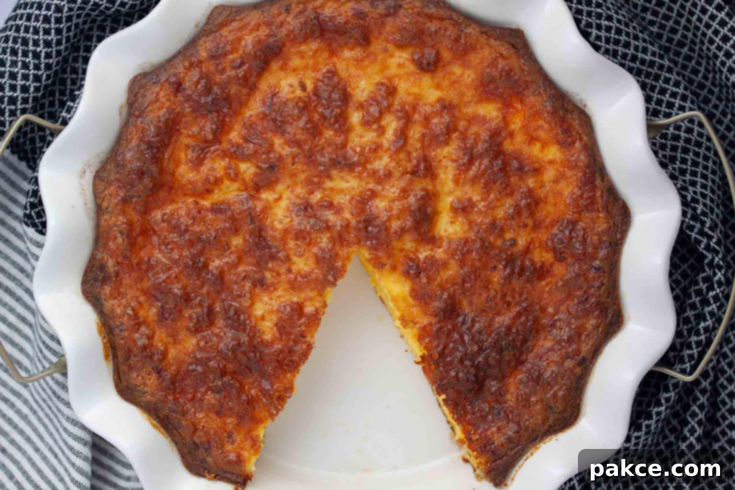 Fluffy Cottage Cheese Quiche 5 Overhead view of a baked crustless quiche in a pie plate, with one slice carefully removed, showing its fluffy, golden-brown texture.