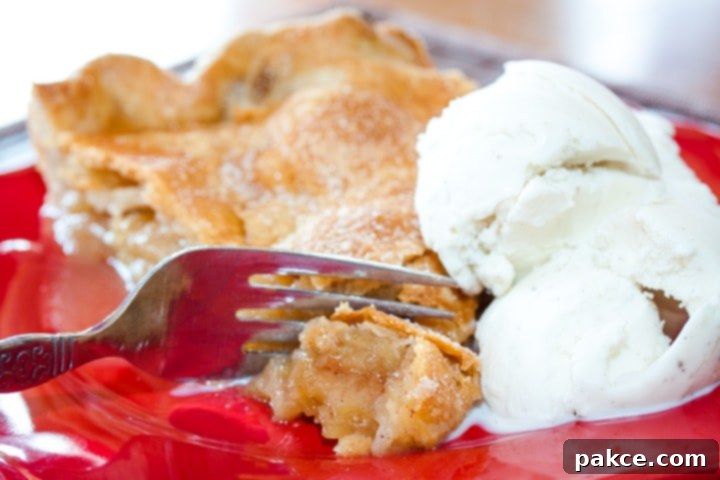homemade-apple-pie-post-horiz-2-min Slice of apple pie with top crust and a scoop of vanilla ice cream with a fork