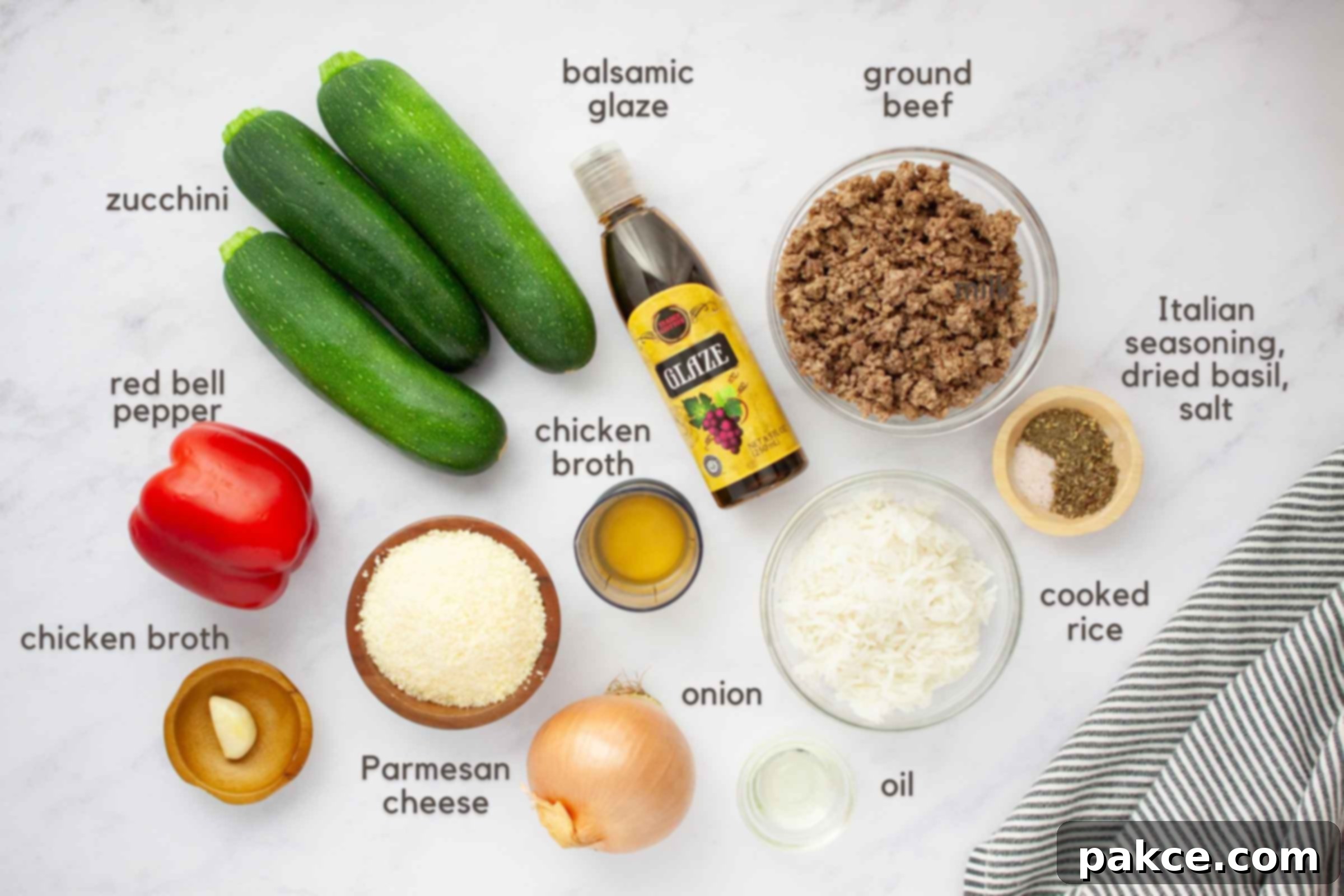 Ground Beef and Rice Stuffed Zucchini Boats 3 Ingredients on a counter: 3 zucchini, 1 red bell pepper, 1 onion, 1 clove garlic, bowl of Parmesan cheese, chicken broth, oil, cooked rice, cooked ground beef, Italian seasoning, dried basil, and salt.