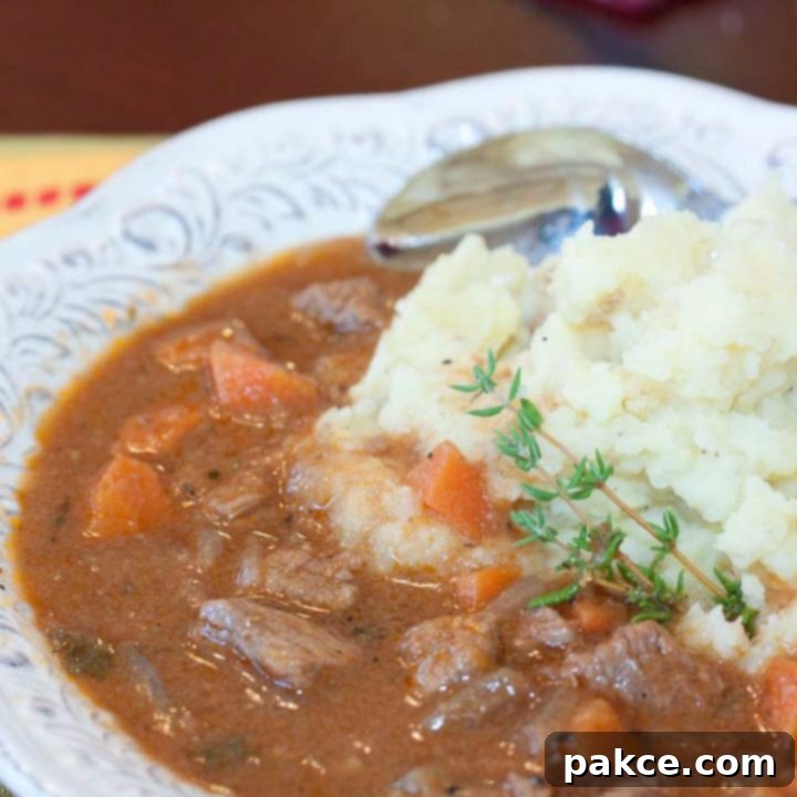 Classic Beef and Guinness Stew served over creamy mashed potatoes, garnished with a sprig of fresh thyme, in a white bowl with a spoon.