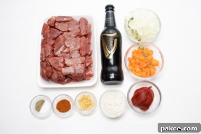 Beef and Guinness Stew A selection of raw ingredients for Beef and Guinness Stew: beef stew meat, a bottle of Guinness beer, chopped onion, sliced carrots, a tube of tomato paste, flour, minced garlic, paprika, dried thyme, salt, and pepper arranged on a wooden surface.