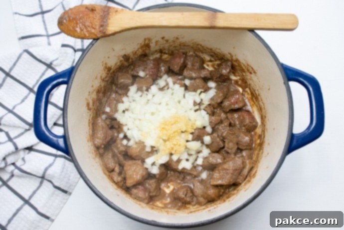 Beef and Guinness Stew Beef stew meat browning in a Dutch oven, with raw chopped onions and minced garlic added to the pot.