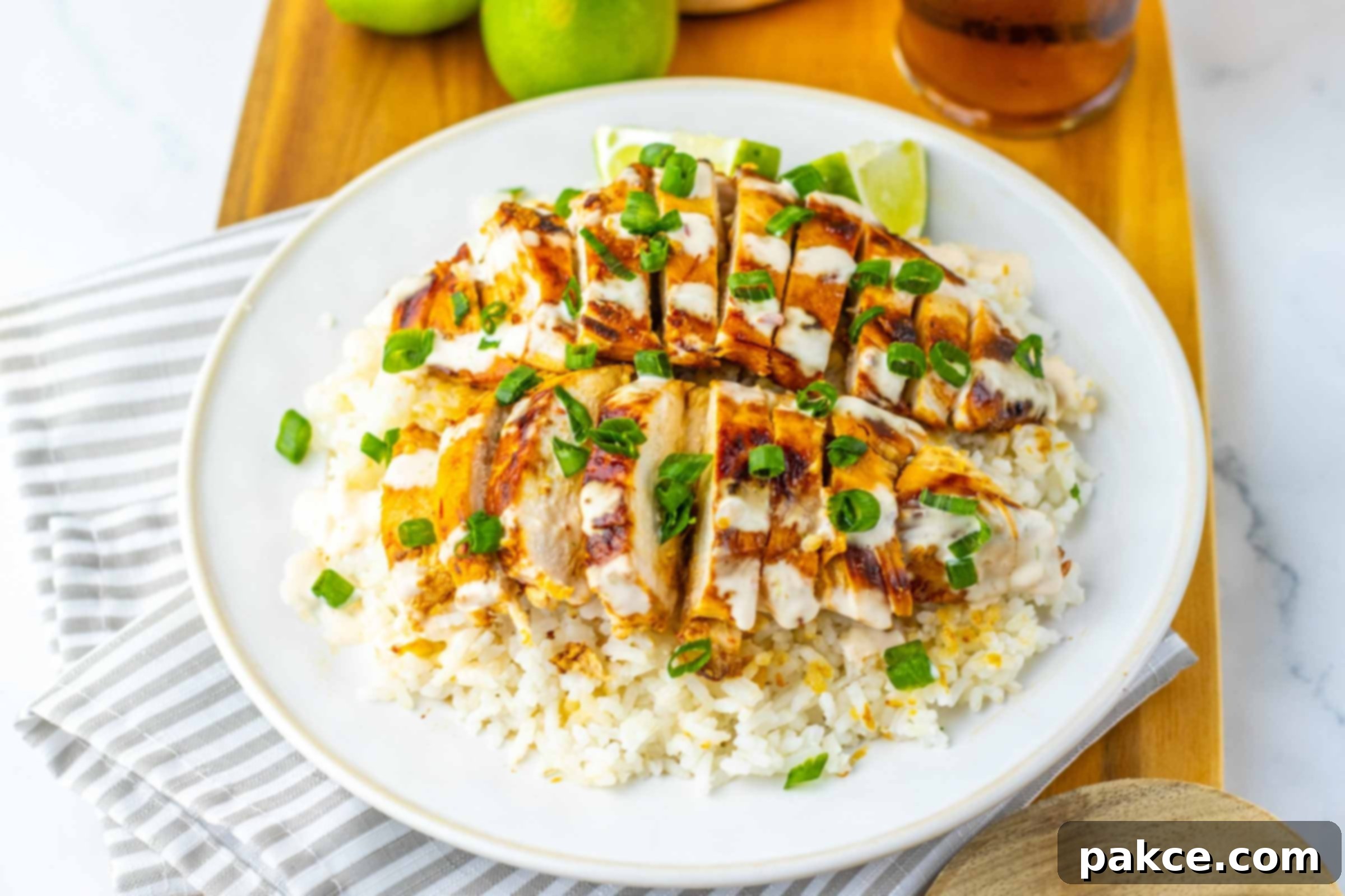 Chicken breast over rice drizzled with white sauce and garnished with green onions beside a glass of iced tea and two limes.