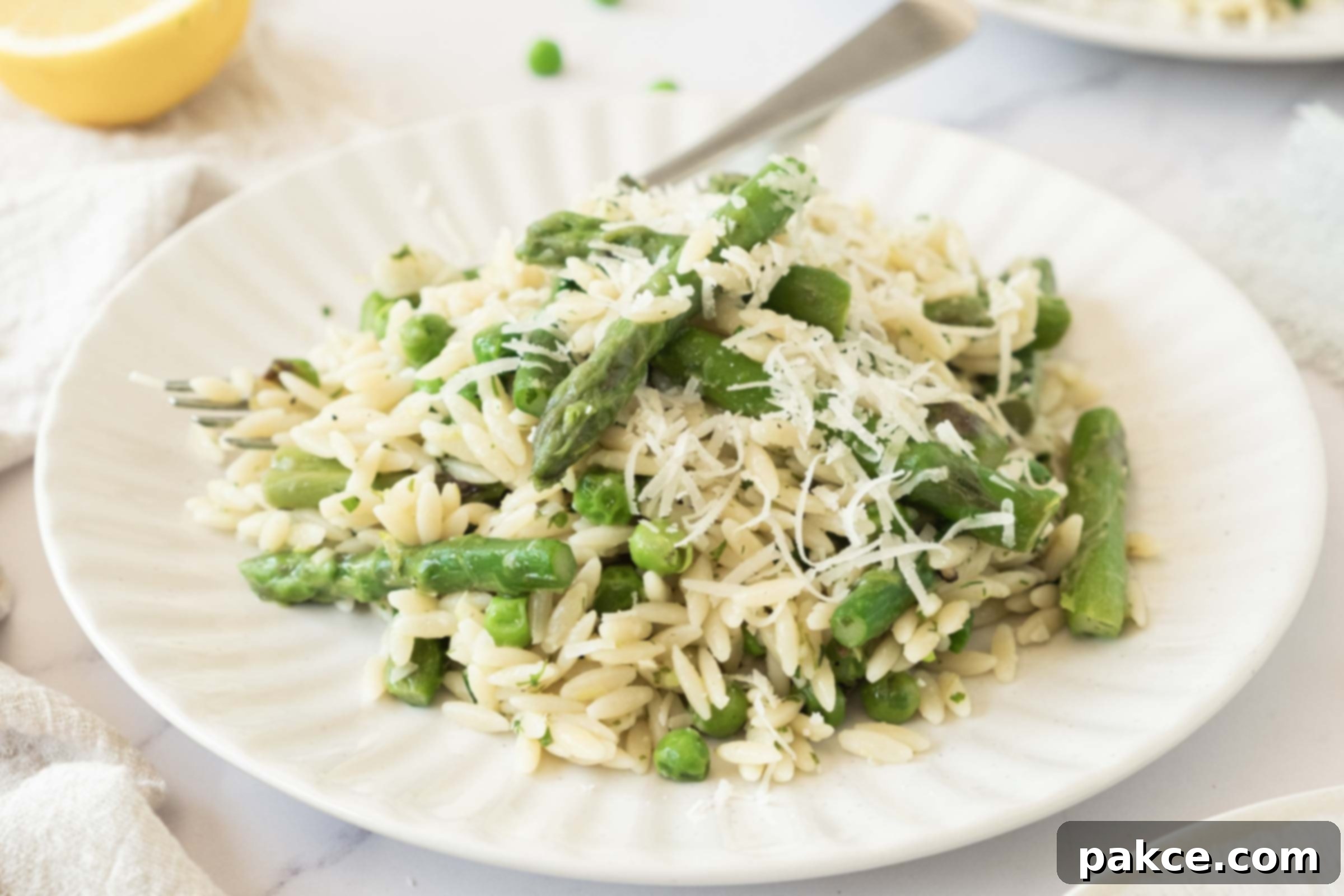 Plate of lemon orzo with peas and asparagus garnished with grated Parmesan cheese, highlighting its fresh and vibrant appeal.