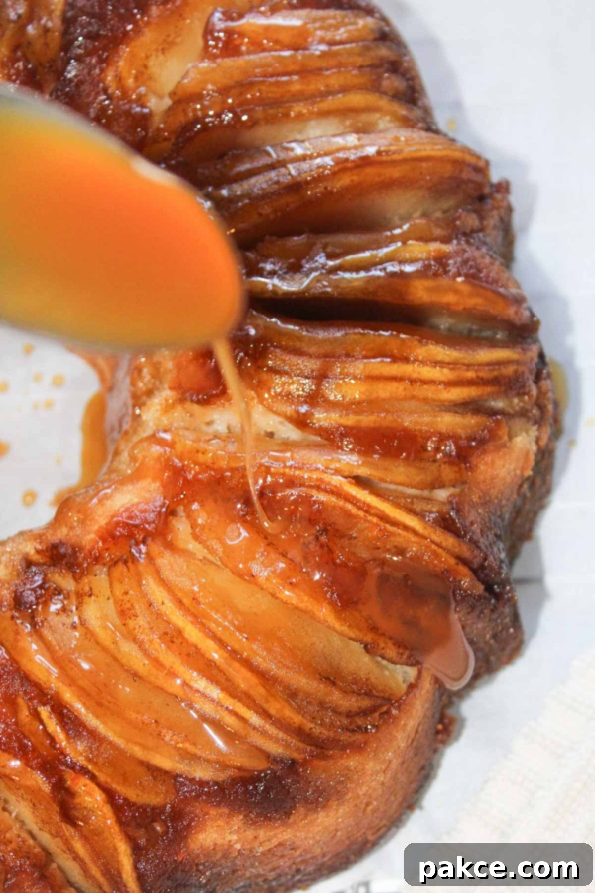 Caramelized Apple Bundt Inversion 10 A close-up shot of a hand drizzling luscious caramel sauce from a spoon over the inverted Caramel Apple Bundt Cake, creating beautiful drips down its sides, emphasizing its rich and inviting appeal.
