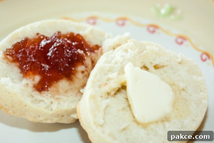 Biscuit cut in half with butter on one half and fruit preserves on the other half on a yellow and white plate