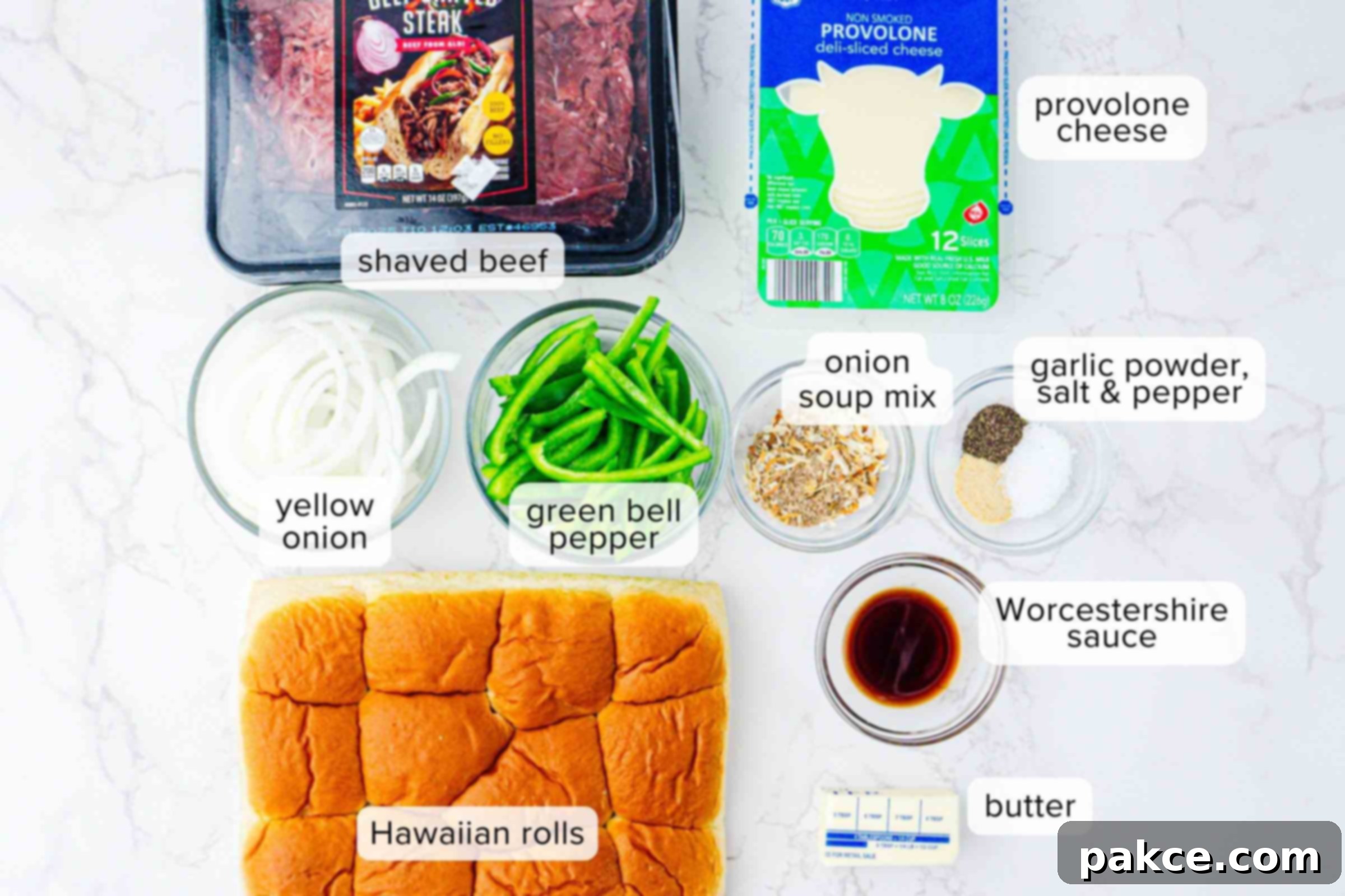Labeled ingredients on a counter: shaved beef, provolone cheese slices, sliced yellow onion, sliced green bell pepper, onion soup mix, garlic powder, salt, pepper, Worcestershire sauce, butter, and Hawaiian rolls, plus cooking oil.