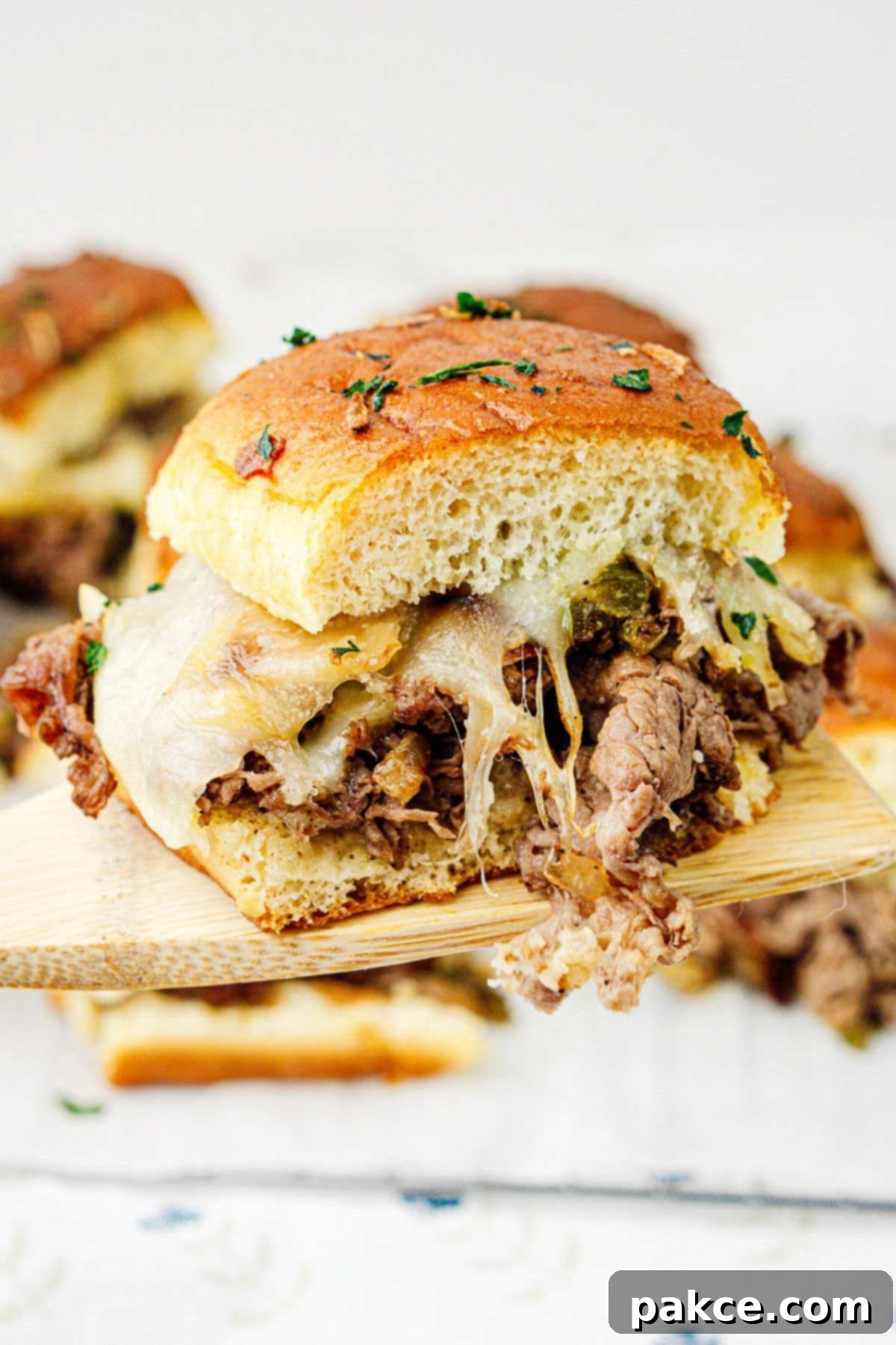 A single Philly cheesesteak slider held up on a wooden spatula.