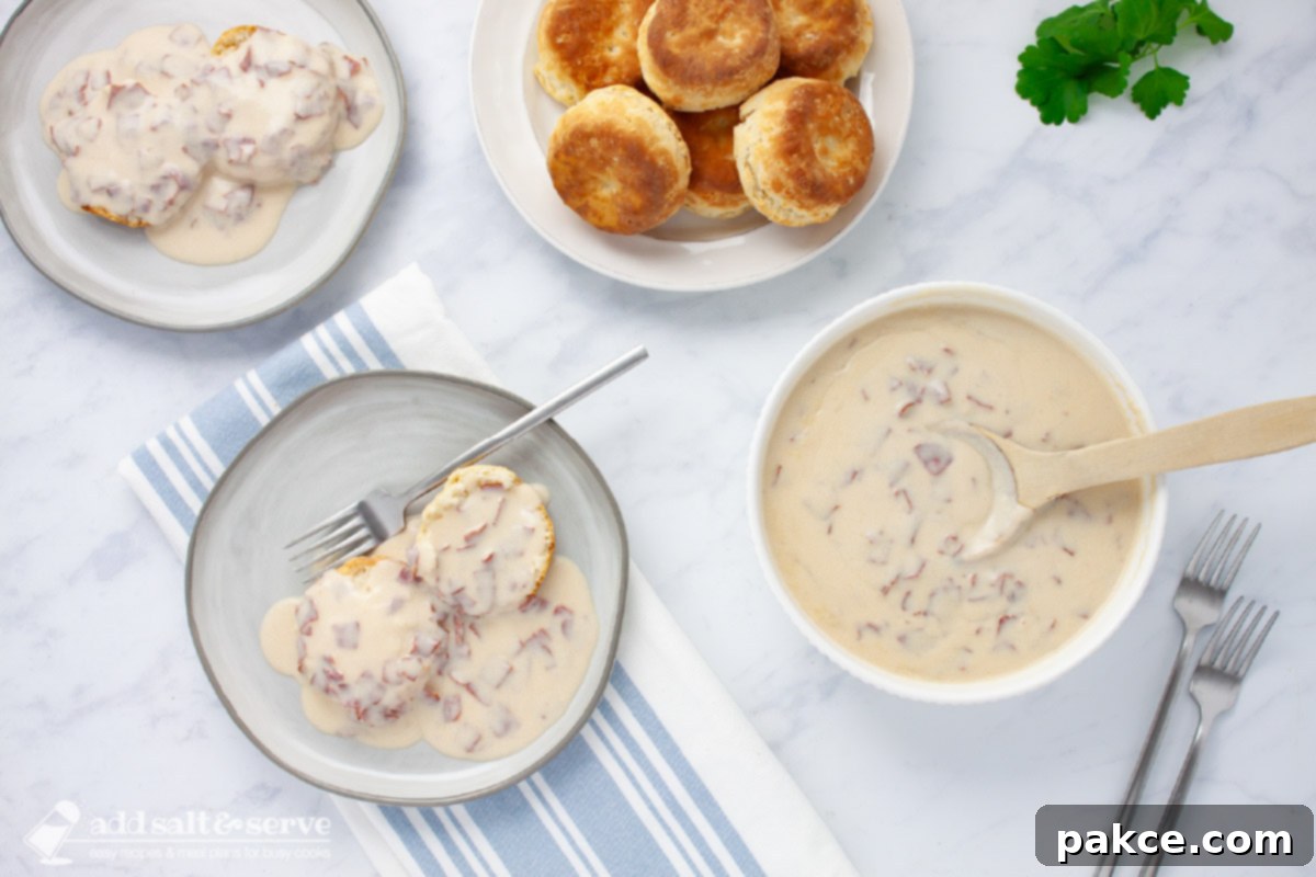 Two plates of creamy chipped beef gravy served over two biscuit halves, with a side bowl of the rich gravy and a wooden spoon, inviting you to a comforting meal.