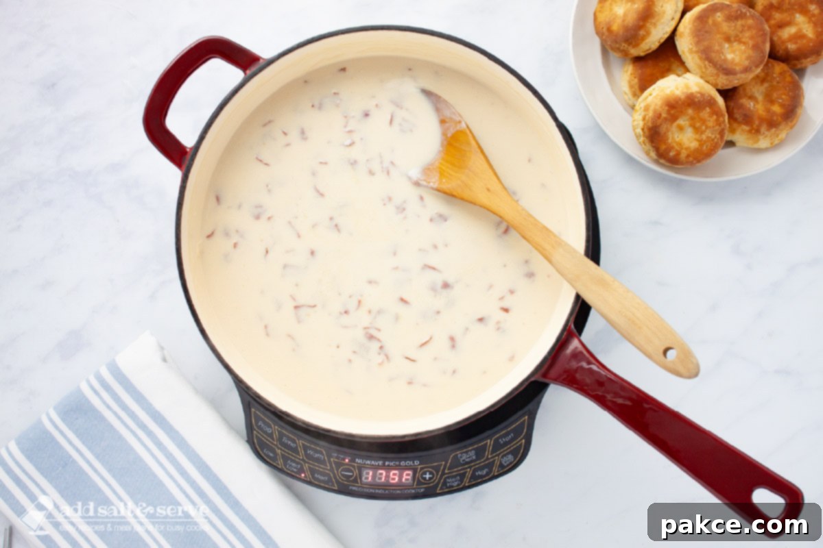Hearty Chipped Beef Gravy 6 A skillet of creamy chipped beef gravy with a wooden spoon, placed next to a plate of freshly baked biscuits, highlighting a rustic and comforting meal.