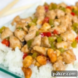 Sichuan Numbing Peanut Chicken 2 Diced chicken and diced red and green bell peppers on a bed of rice on a transparent square glass plate.